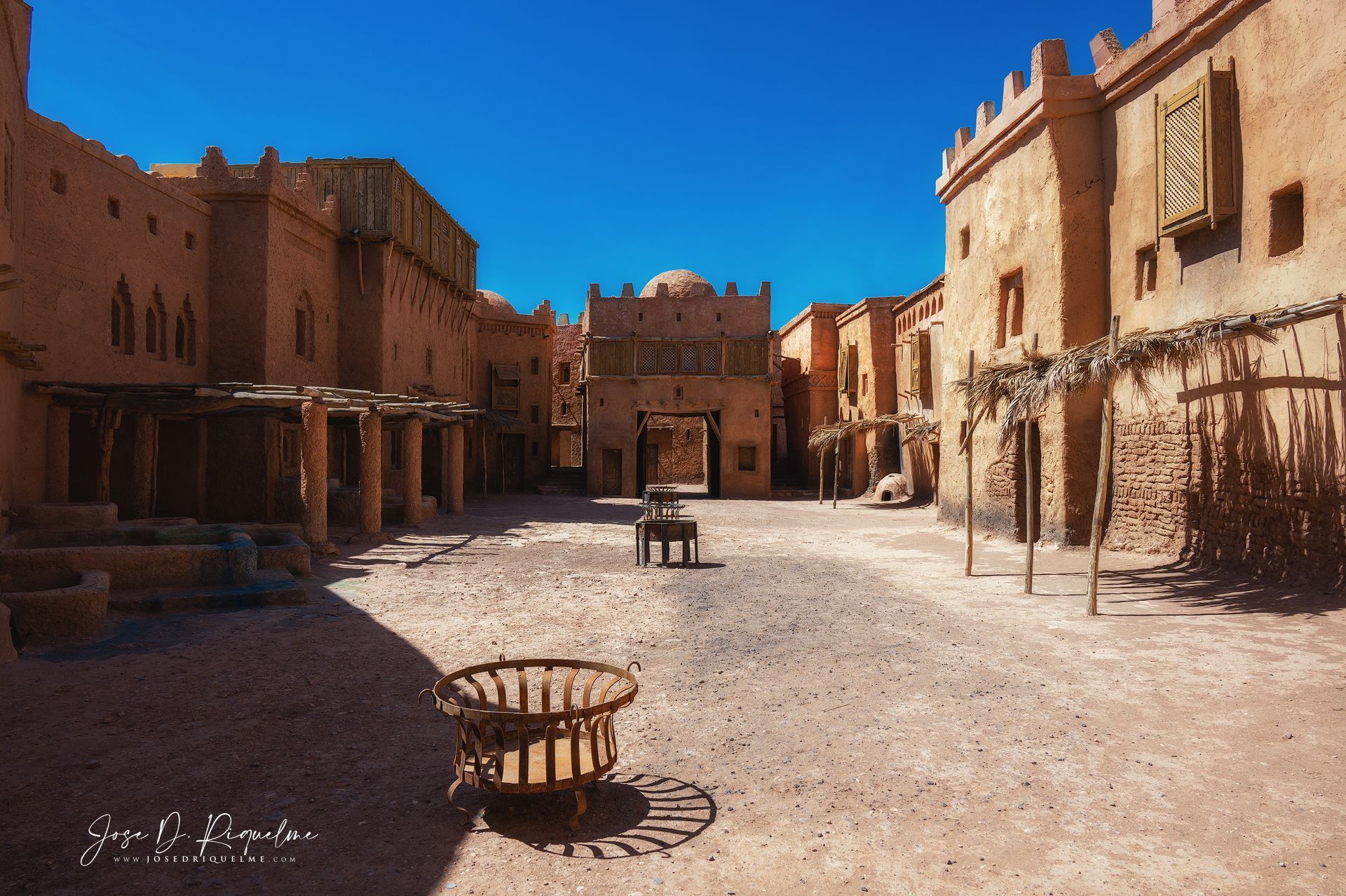 Adobe film set with mud-brick walls and a fire basket under a blue sky at the Ouarzazate film studios, Morocco